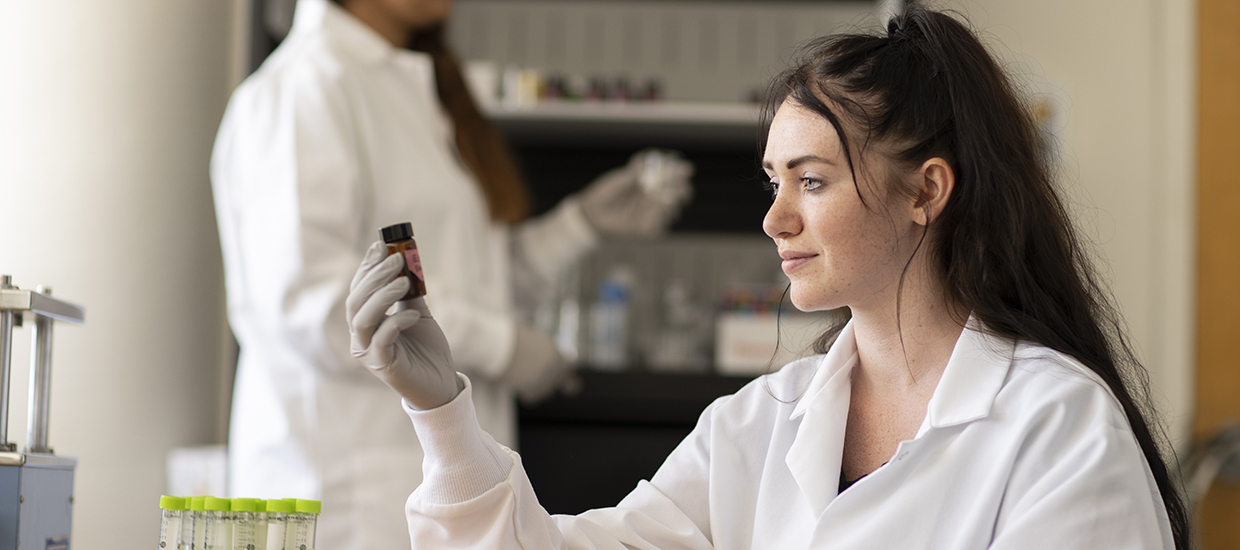 woman sitting at table examining a vial of material